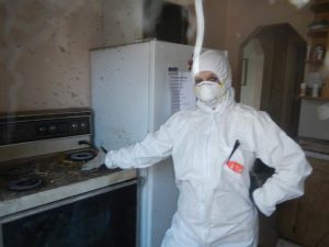 Suited up hazmat cleaner by filthy stove in hoarder home