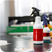 Close-up of cleaning spray bottles on a table, ready for use in a cleaning process, with a blurred background of a workspace.