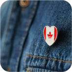Close-up of a heart-shaped pin with the Canadian flag design, attached to the pocket of a denim jacket, showing patriotism and style.