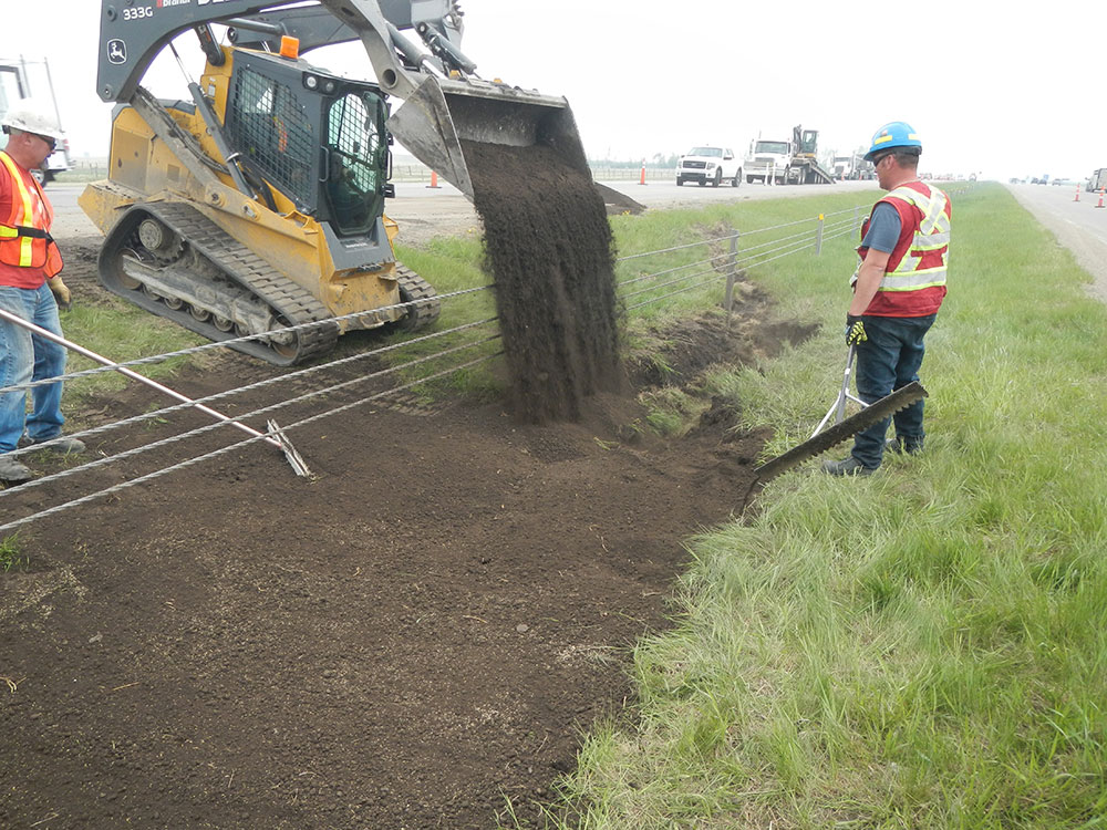 Workers using a loader to pour soil during a special spill cleanup along the roadside, highlighting the importance of proper spill management for safety.